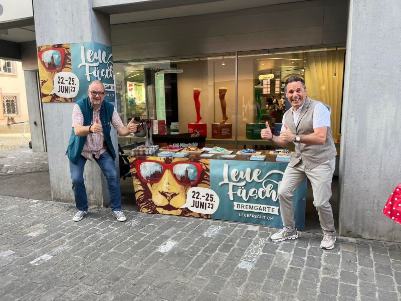 Foto zweier Festbändel-Verkäufer vor ihrem Marktstand. Foto zweier Festbändel-Verkäufer vor ihrem Marktstand.